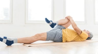 Senior man performing a leg stretching exercise on a yoga mat.